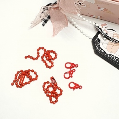 Acessórios vermelhos de plástico, correntes e ganchos, com caixa decorada e fitas ao lado