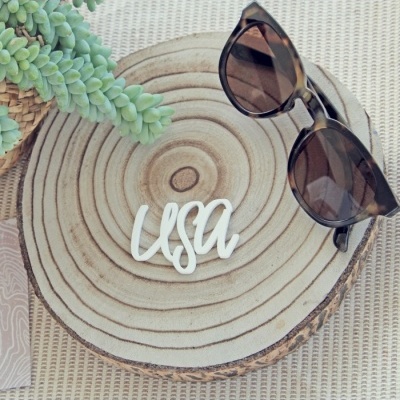 Óculos de sol castanhos e lentes escuras sobre fatia redonda de madeira com palavra 