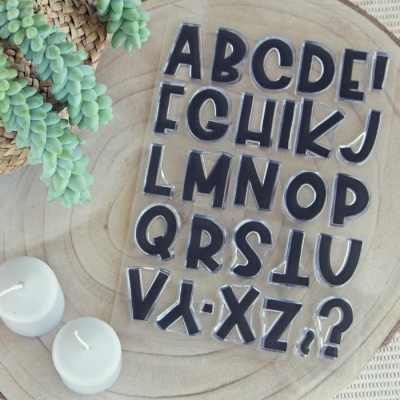 Carimbos alfabéticos pretos em base transparente sobre madeira com velas e plantas suculentas