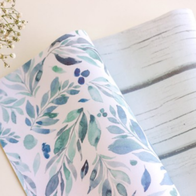 Dois rolos de papel decorativo com padrões de folhas e listras, sobre superfície clara