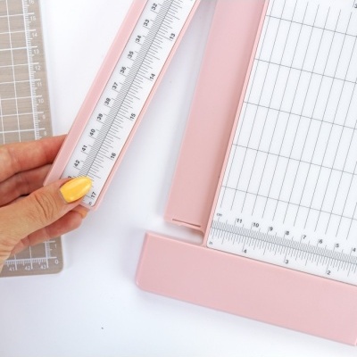 Mão segurando régua transparente sobre cortador de papel rosa