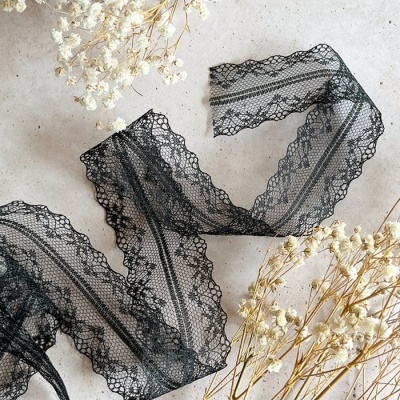 Fita de renda preta com padrão floral ao lado de flores secas brancas