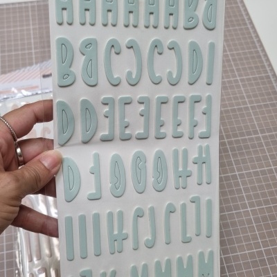 Folha de autocolantes em forma de letras maiúsculas azul esverdeadas em relevo numa embalagem plástica