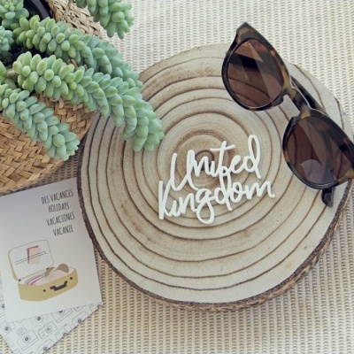 Óculos de sol castanhos escuros sobre base de madeira redonda com planta verde e cartão de férias