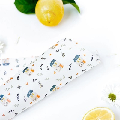 Pano branco com padrão de casinhas coloridas e folhagem, limão e flores ao redor