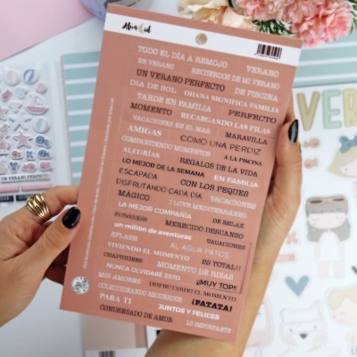 Folha autocolante com frases positivas em espanhol em cor castanha clara e texto branco segurada por mãos femininas