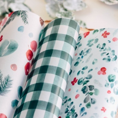 Rolos de papel de embrulho com padrões natalícios em cima de mesa de madeira