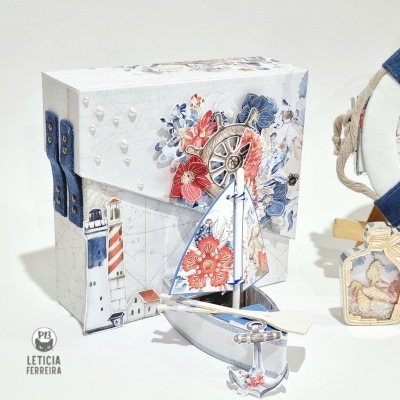 Caixa decorativa náutica com farol e flores, acompanhado por mini barco de vela decorativo