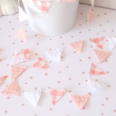 Guirlanda decorativa em triângulos de tecido rosa e branco sobre superfície com bolinhas cor-de-rosa