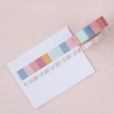 Fita adesiva decorativa colorida em papel branco sobre mesa rosa clara