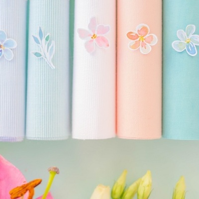 Toalhas coloridas enroladas com bordados florais em fundo claro com flores naturais