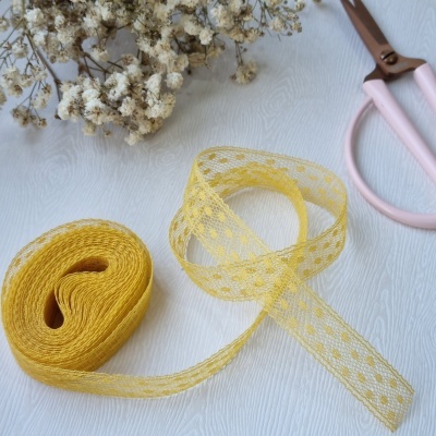 Fita rendada amarela com padrão floral ao lado de flores secas e tesoura rosa