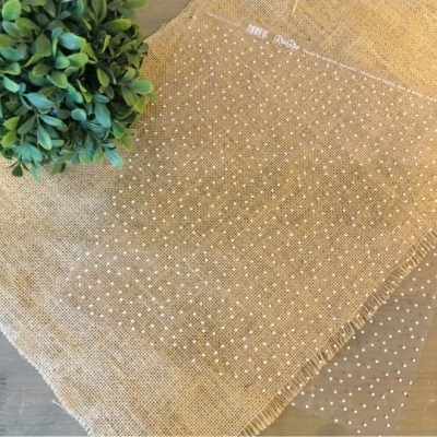 Saco transparente com bolinhas brancas sobre pano de juta com planta verde ao lado