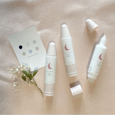 Três tubos de creme branco com desenho de lua, flores e cartolina com círculos coloridos sobre tecido bege