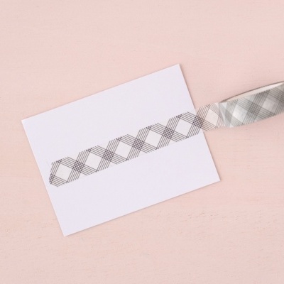 Fita decorativa autocolante com padrão xadrez cinzento e branco sobre papel branco