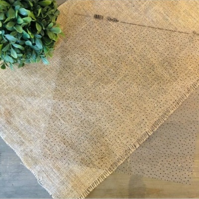 Tecido de juta cru sobre mesa de madeira com padrões pontilhados e ramo verde artificial