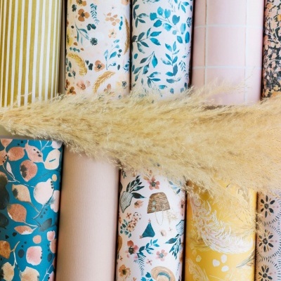 Rolos de papel decorativo com padrões coloridos e um ramo de planta seca por cima