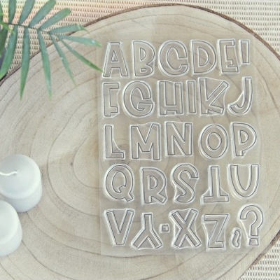 Conjunto de carimbos de letras transparentes sobre base de madeira com velas brancas e folha verde