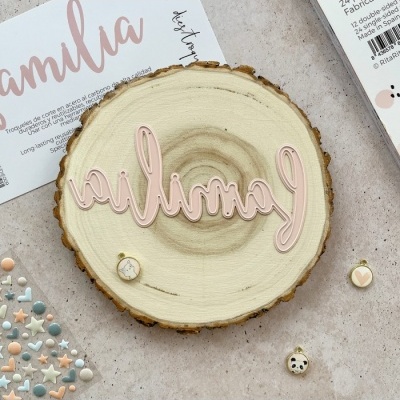 Placa decorativa de madeira redonda com palavra 'família' em rosa claro e pequenos itens decorativos ao redor