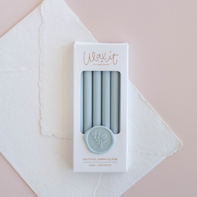 Conjunto de varetas de cera cinza em embalagem branca com selo decorativo e fundo de papel