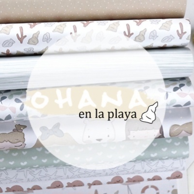 Rolos de papel de embrulho com padrões de conchas e corações em tons pastéis e texto 'OHANA en la playa'.