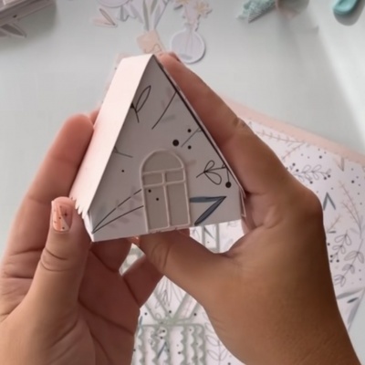 Miniatura de casa de papel branca com desenhos pretos e triângulo azul nas mãos