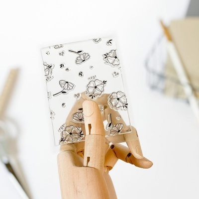 Mão de manequim de madeira segurando cartão floral e borboletas preto sobre branco