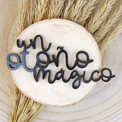 Adorno metálico preto com a frase 'un otoño mágico' sobre base de madeira e plantas secas