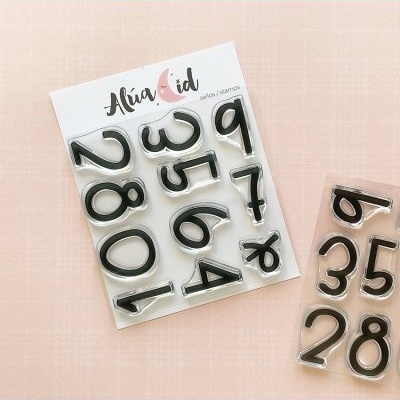 Selos de números em silicone preto da Alúa Cid sobre fundo rosa claro