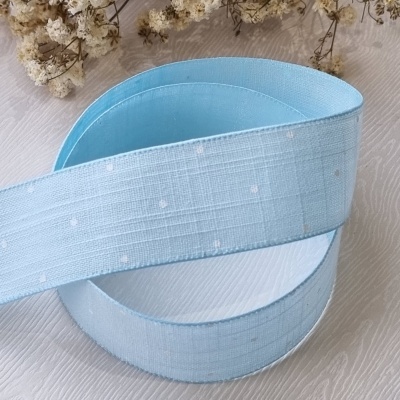 Fita azul clara com pequenos pontos brancos sobre superfície branca com flores secas ao fundo