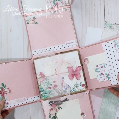 Caixa de papel rosa decorada com flores, borboleta e pássaro em fundo de madeira clara