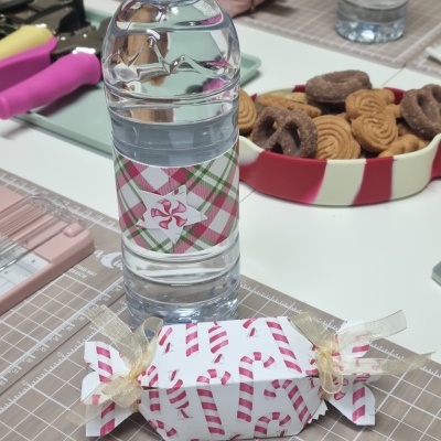 Garrafa de água decorada e caixa de presente com padrão de bengalas de doces vermelhas sobre mesa