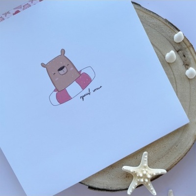 Folha branca com desenho de urso com boia, sobre tronco de madeira com estrela-do-mar e conchas