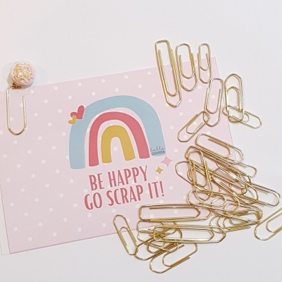 Cartão rosa claro com arco-íris e texto e vários clipes de papel dourados