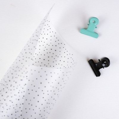 Papel transparente com estrelas pretas e dois clipes coloridos sobre fundo branco