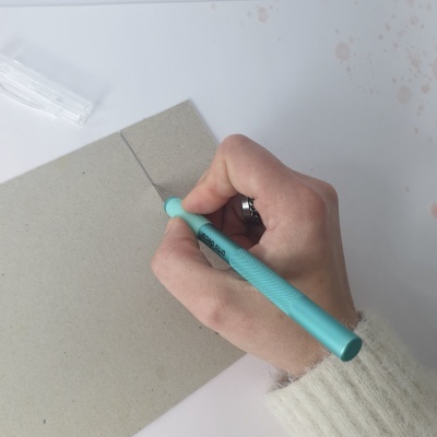 Mão a cortar papelão com estilete azul claro sobre mesa branca