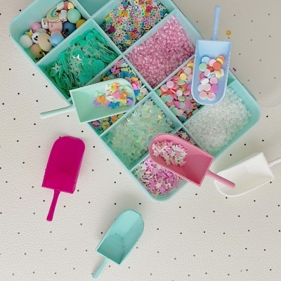 Recipientes com confetes coloridos e pás de plástico sobre superfície branca