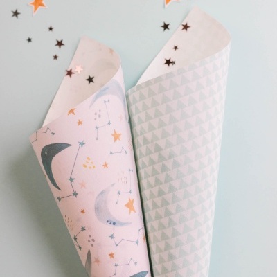 Dois rolos de papel de embrulho com padrões de luas e triângulos sobre superfície cinza