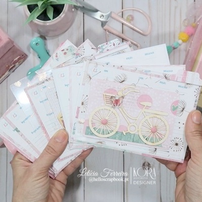 Cartões decorativos com bicicleta e balões em mãos, caixa rosa, ferramentas e bloco de notas com palavra FELIZ