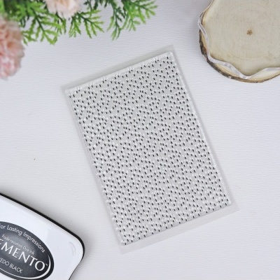 Carimbo transparente com padrão de pontos pretos numa mesa branca com tinteiro e flores