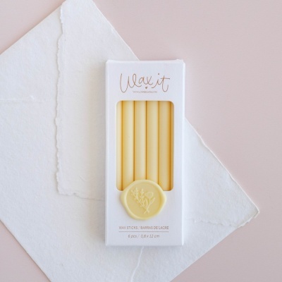 Palitos de lacre amarelos na embalagem branca sobre papéis brancos e fundo rosa