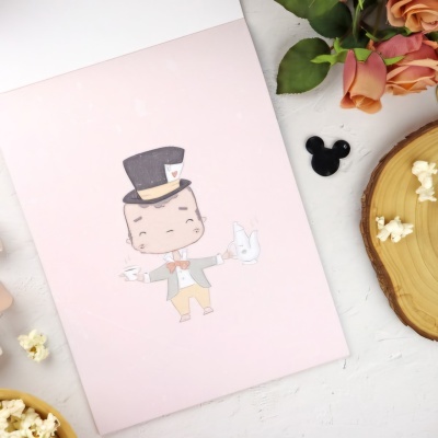 Caderno rosa com desenho de homem de cartola, botão preto Mickey, flores e fatia de madeira com pipocas