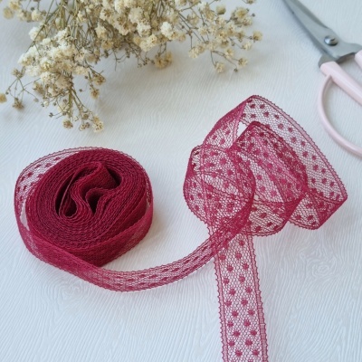 Fita de renda vinho com padrão de pontos ao lado de flores secas e tesoura