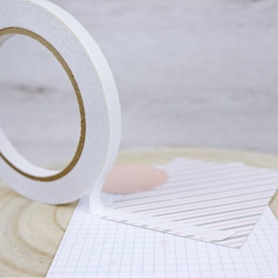 rolo de fita adesiva dupla face branca sobre mesa de madeira com papéis ao lado