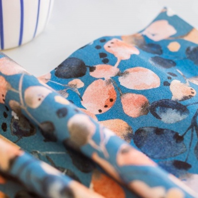 Tecido com padrão floral colorido junto a caneca branca com riscas azuis