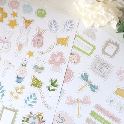 Folhas autocolantes com desenhos coloridos de coelhos, flores, libélulas e texto em português e espanhol
