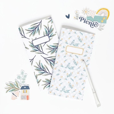 Dois cadernos decorados com folhas, marcador branco e recortes de papel coloridos com o texto Picnic.