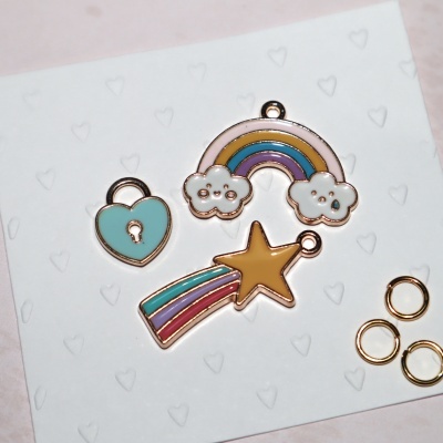 pendentes coloridos de metal com coração, arco-íris e estrela sobre cartão branco com corações em relevo