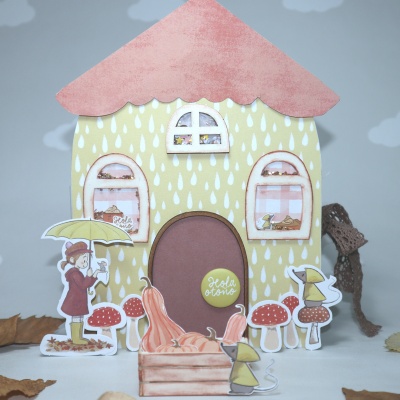 Casinha decorativa de papel com telhado rosa e figuras de crianças e cogumelos