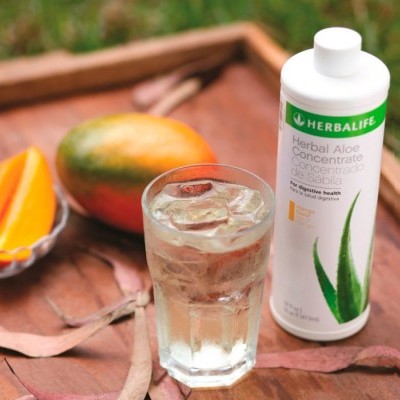 Suplemento Herbal Aloe Concentrate Herbalife com copo de bebida, fatias de manga e bandeja de madeira